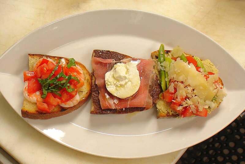 Top view of three pieces of bread topped with seafood, meat and vegetables